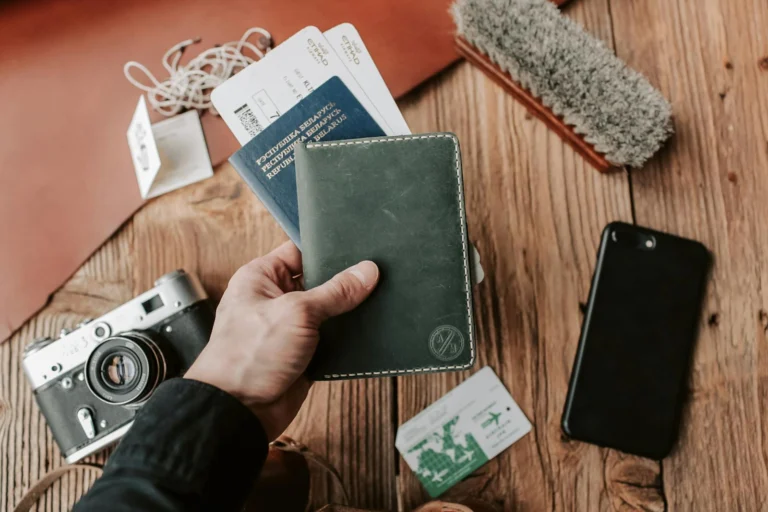 Mao segurando passaporte com itens essenciais de viagem sobre a mesa