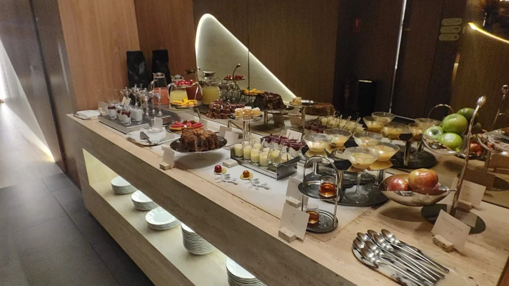Buffet da Taste of Priceless no Terminal 3 do GRU, com luminárias esculturais e seleção de pratos, doces e frutas