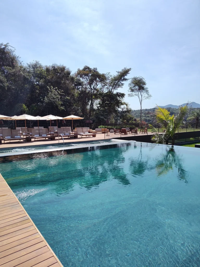 Deck da piscina do Hotel Clara em Inhotim, com espreguiçadeiras e guarda-sóis voltados para a piscina de borda infinita