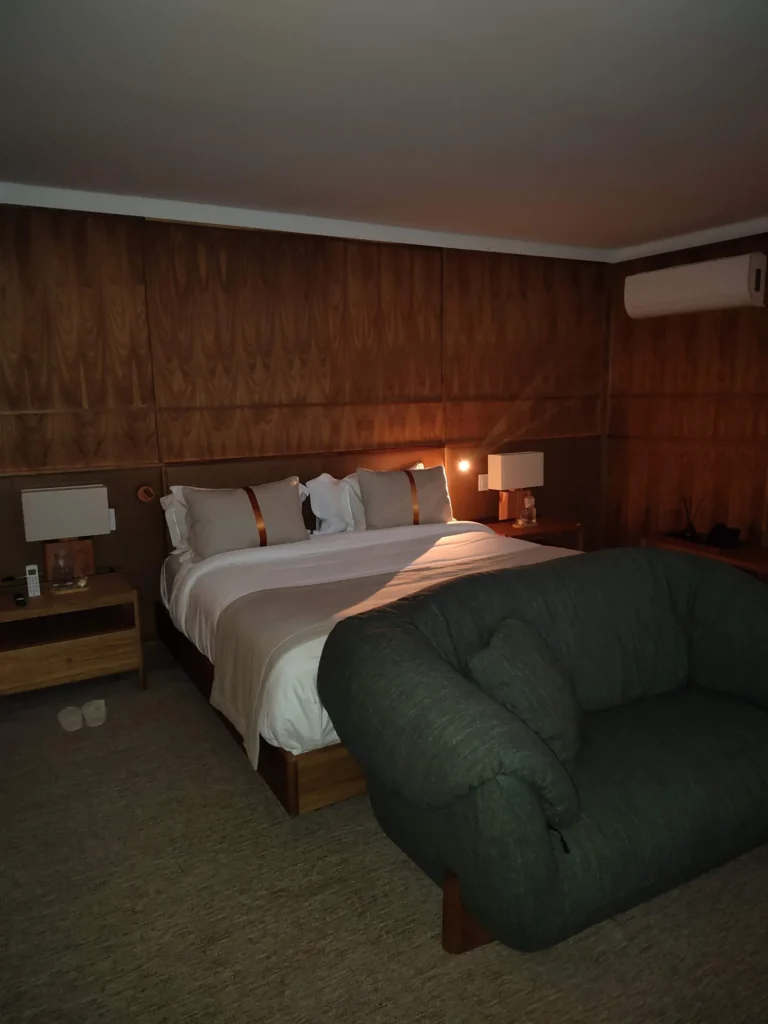 Suíte do Hotel Clara em Inhotim, com painéis de madeira e poltrona de design brasileiro