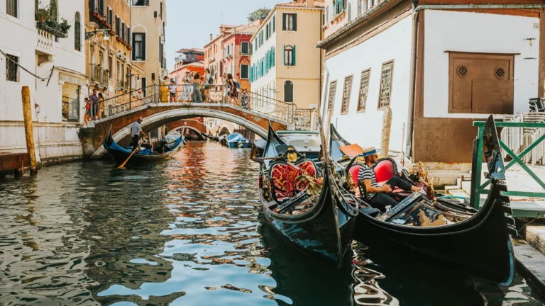 Gôndolas em um canal de Veneza, com ponte e casario colorido ao fundo