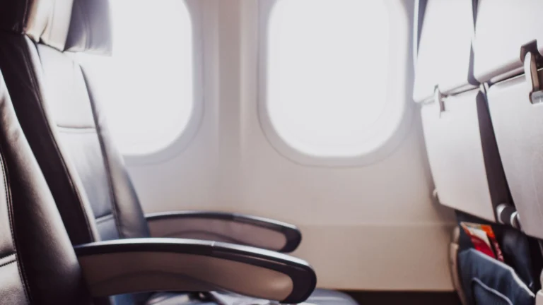 Poltronas de couro junto às janelas de uma cabine de avião iluminada pela luz natural.