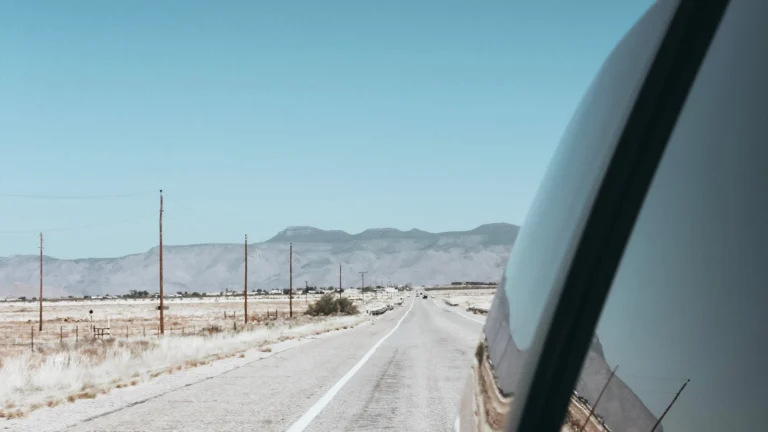Vista de dentro do carro em uma estrada deserta do Arizona, com montanhas ao fundo, em uma road trip pelos Estados Unidos.