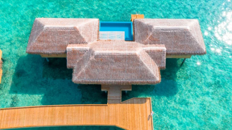 Bangalô sobre a água com telhado de palha e piscina privativa em lagoa de águas turquesa cristalinas nas Maldivas.