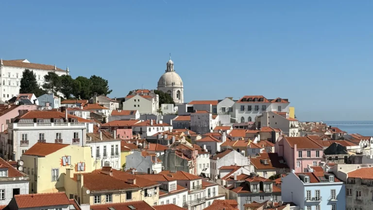 Vista aérea dos telhados de terracota da Alfama com a cúpula do Panteão Nacional e o rio Tejo ao fundo, em Lisboa, Portugal.
