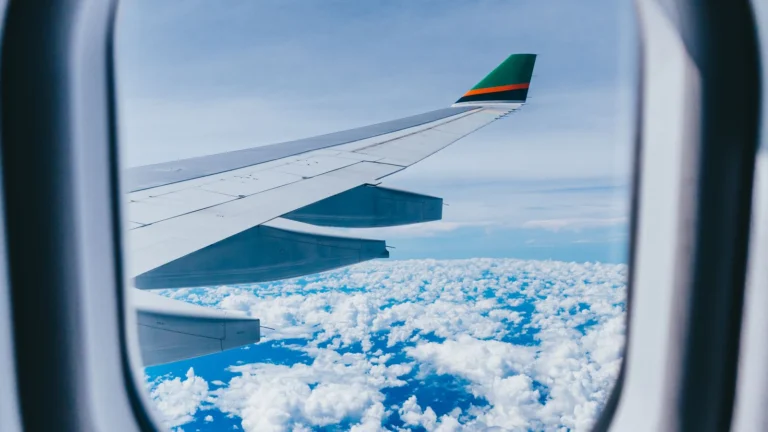 Vista da asa do avião sobre um mar de nuvens pela janela, em voo internacional de longa distância.