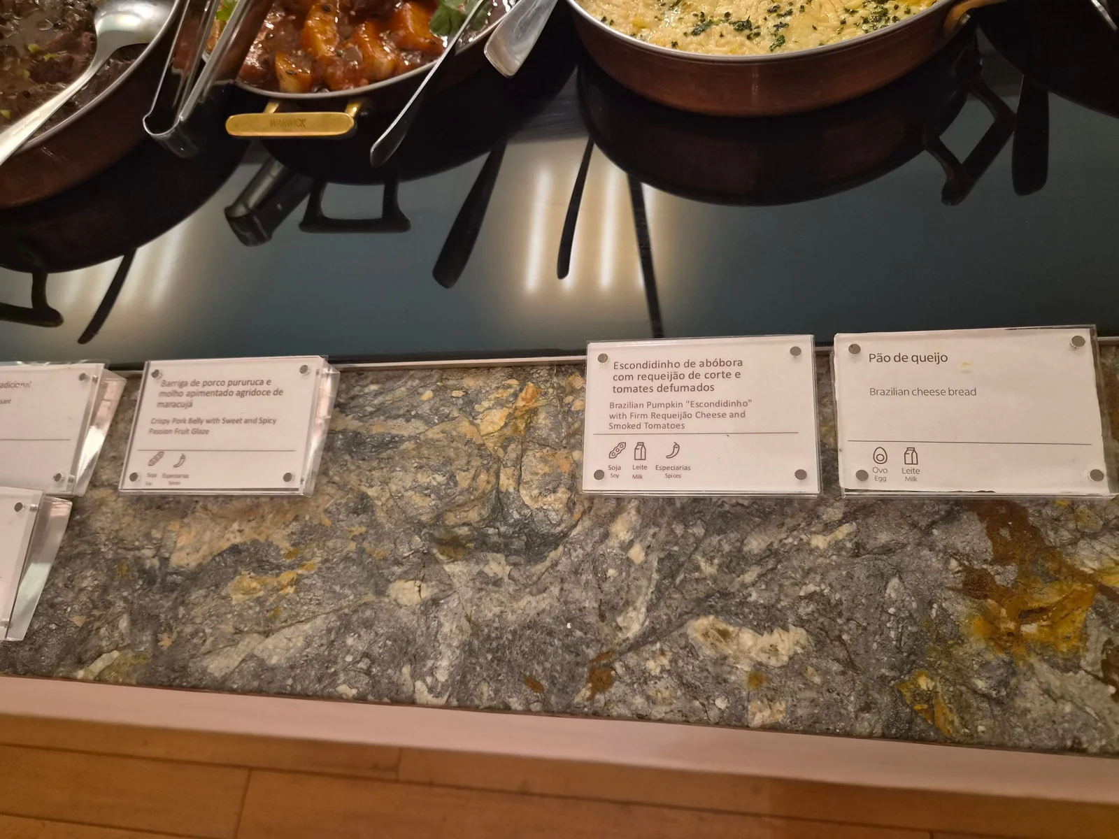 Placas de identificação dos pratos no balcão da Sala Pedra Preta: barriga de porco pururuca e escondidinho de abóbora