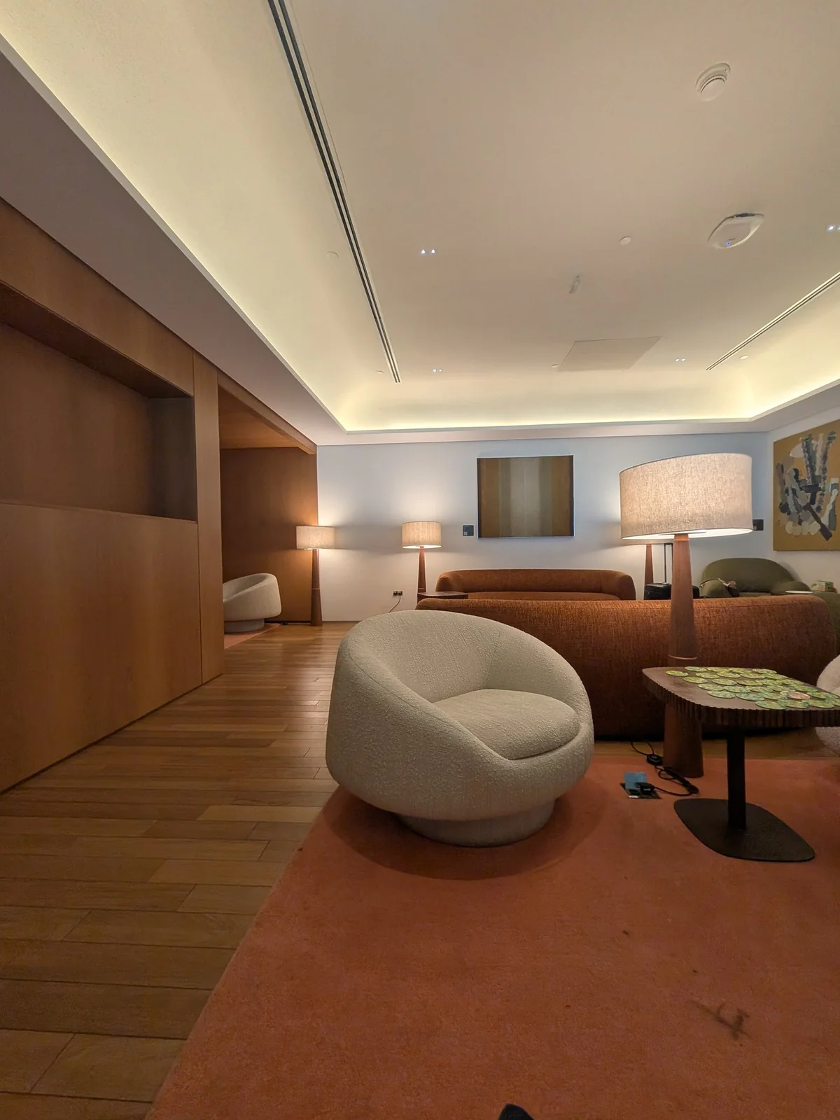 Área de estar com poltrona giratória branca em tecido bouclé, sofá curvo terracota e luminárias de design na Sala Pedra Preta