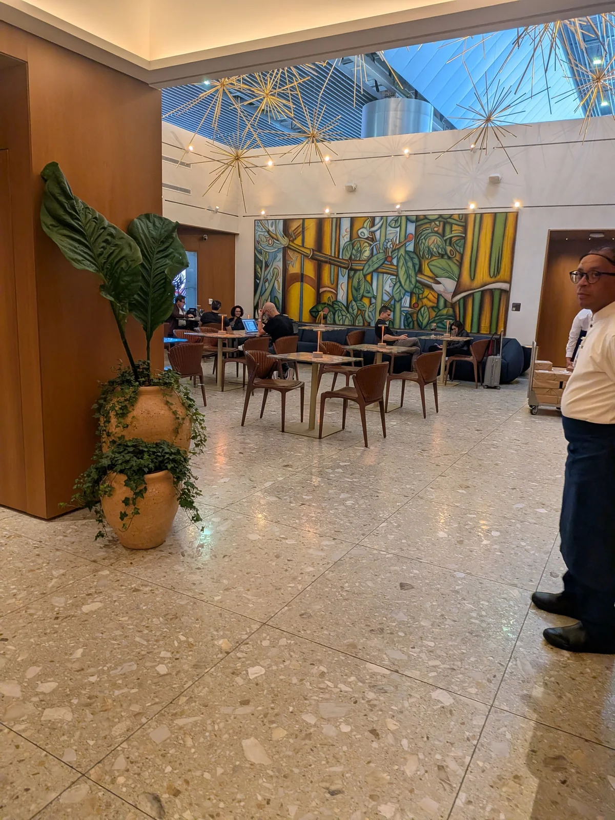 Salão gastronômico da Sala Pedra Preta com pé-direito duplo, imenso mural de arte brasileira modernista e luminárias douradas